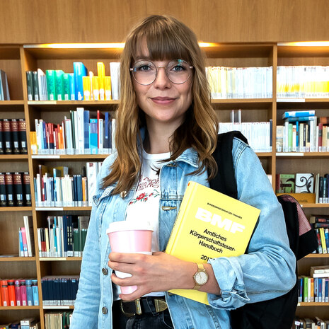  Junge Frau mit Fachbuch in einer Bibliothek